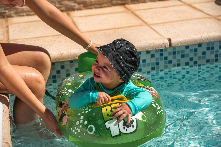 Adorable baby in a float enjoying a sunny pool day while being supported by an adult.